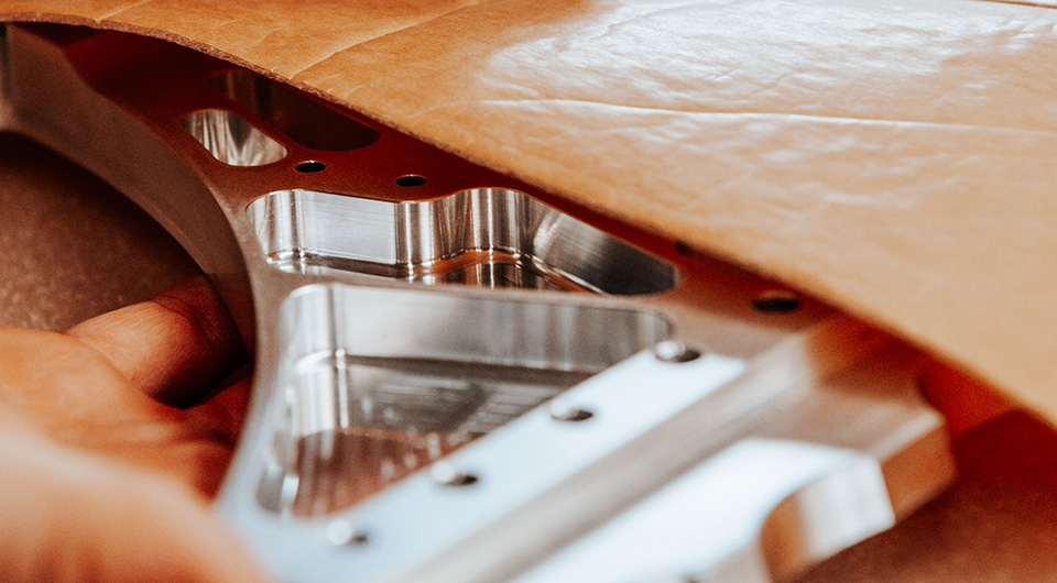 Main en train de tenir une pièce métallique usinée sous un matériau marron.