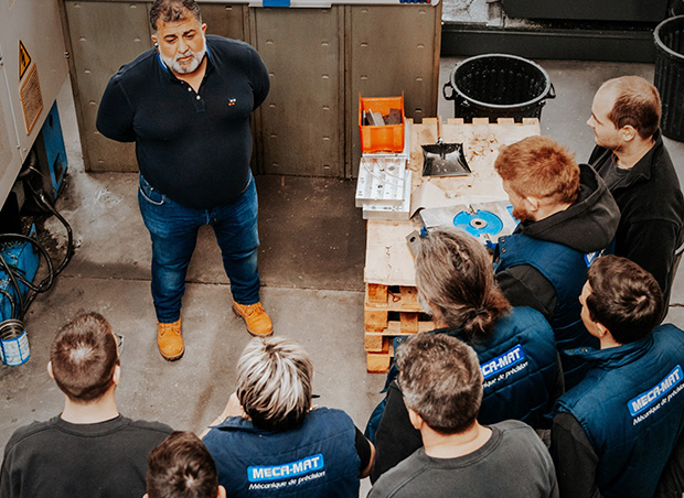 Un homme explique un processus à des ouvriers attentifs dans un atelier.